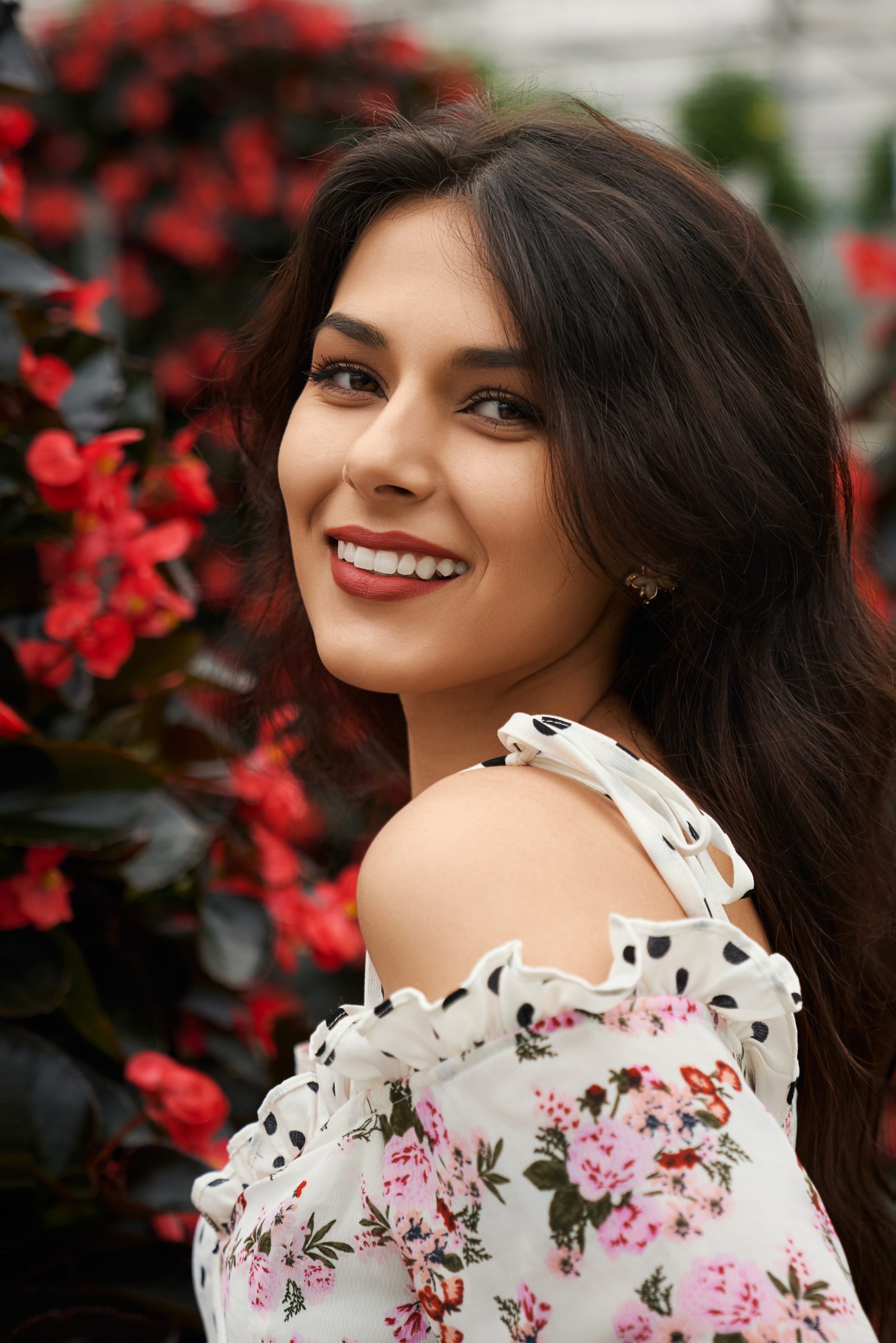 Portrait of smiling beautiful brunette woman in cute dress and in red lips on flowers background. Concept of professional photossesion in modern greenhouse.