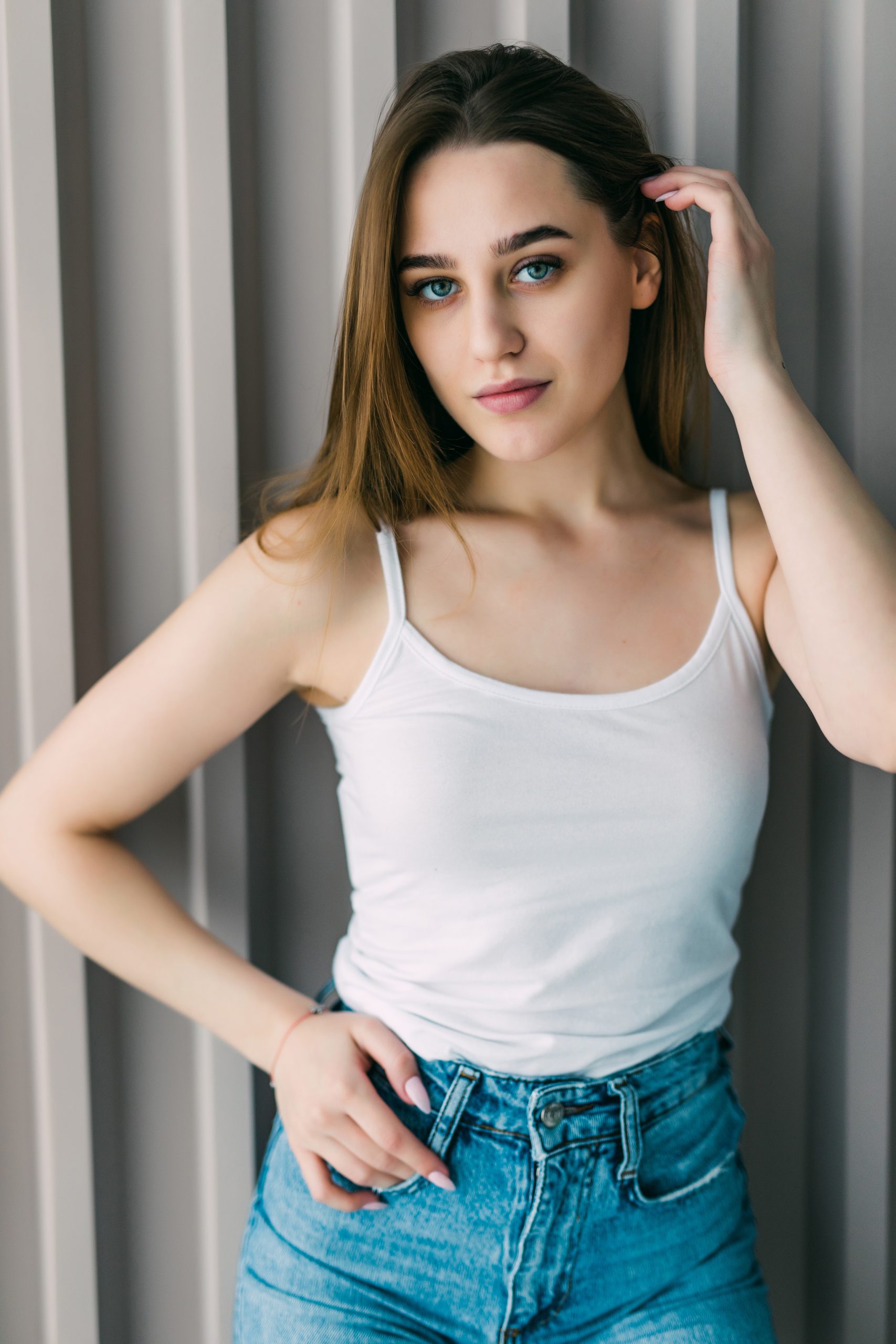 Stylish young woman standing in loft apartment, looking at camera, smiling hand in hair.